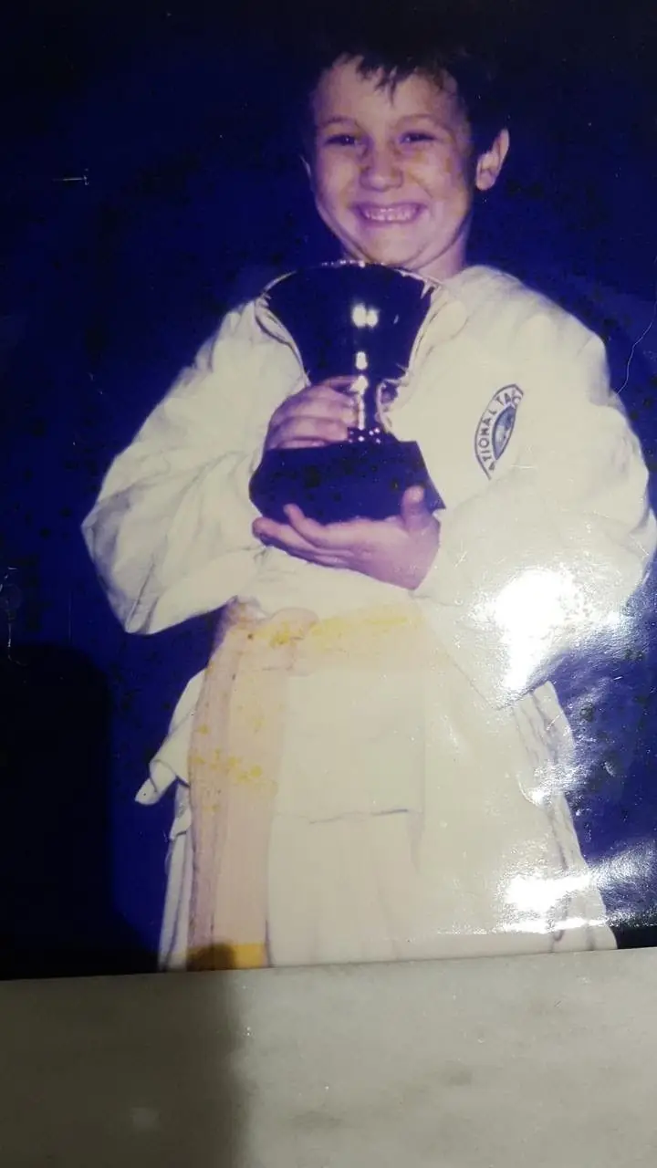 Daniel Flash as a boy in a white uniform holding a trophy