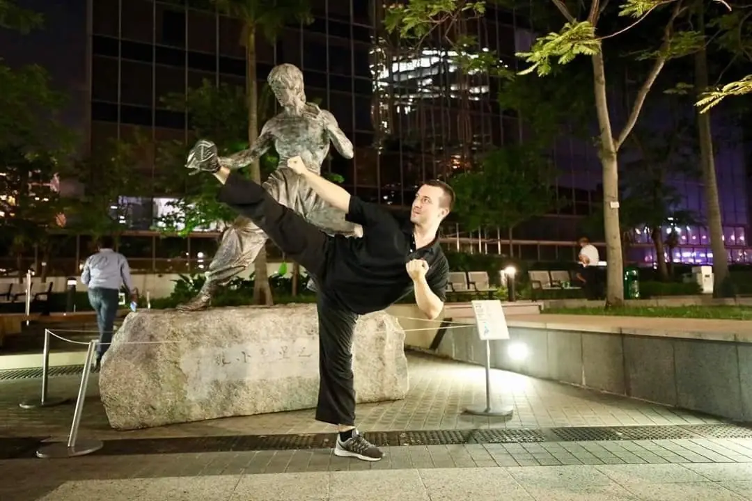 Daniel Flash kicking beside the Bruce Lee statue at night