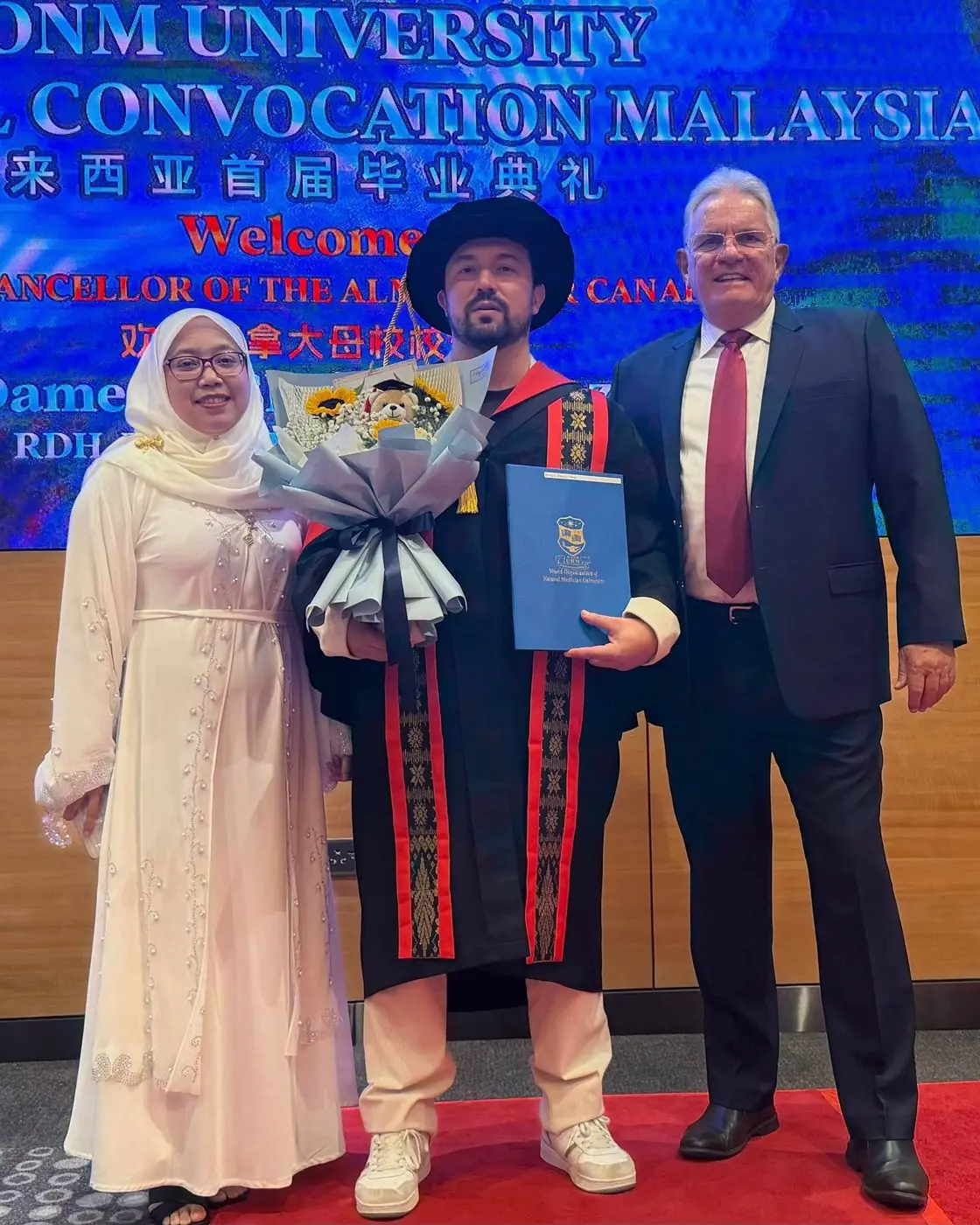 Dr. Daniel Flash on stage at the WONM University convocation holding flowers and his diploma